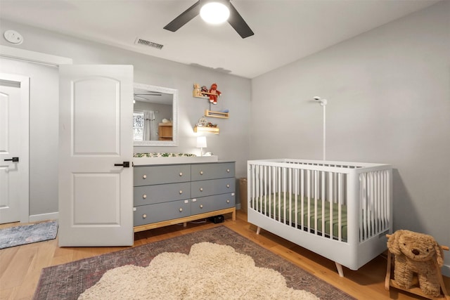 bedroom with a nursery area, wood finished floors, visible vents, and a ceiling fan