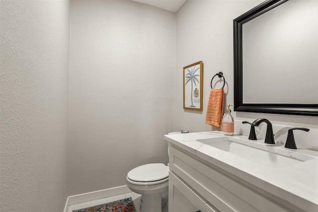 half bath with baseboards, a textured wall, vanity, and toilet