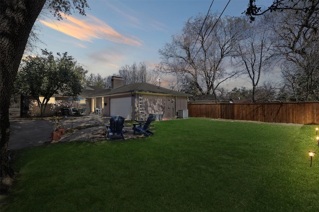 yard at dusk with an attached garage, fence, and cooling unit