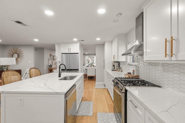 kitchen featuring visible vents, an island with sink, wall chimney exhaust hood, stainless steel appliances, and a sink