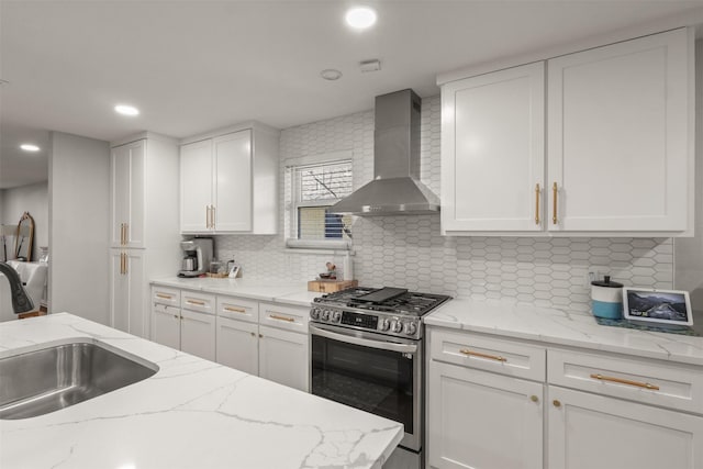 kitchen featuring wall chimney exhaust hood, white cabinetry, a sink, and gas stove