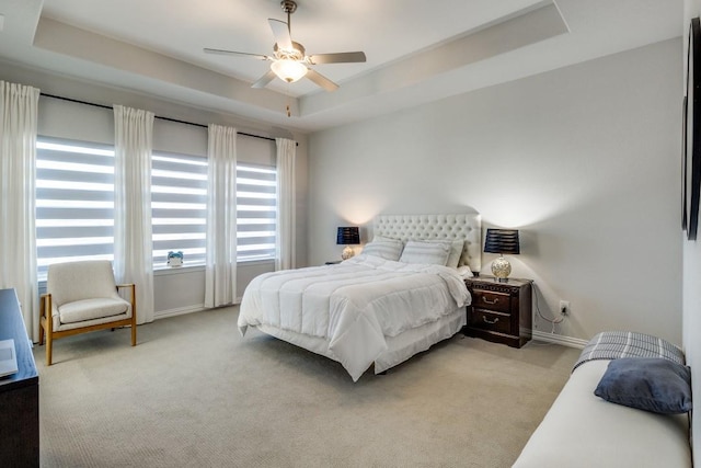 carpeted bedroom featuring multiple windows, a raised ceiling, a ceiling fan, and baseboards