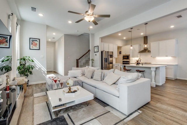 living area featuring recessed lighting, visible vents, light wood finished floors, and stairs