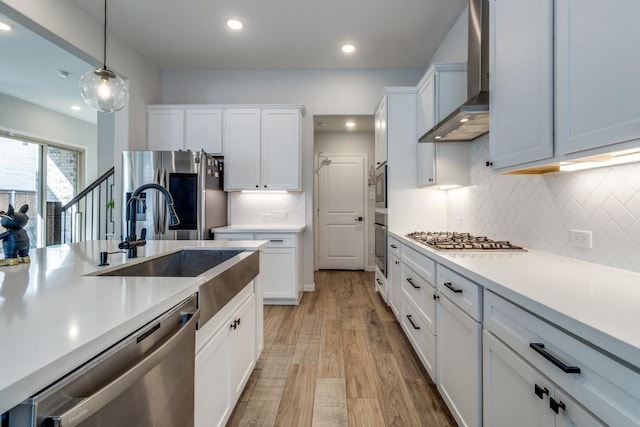 kitchen with pendant lighting, stainless steel appliances, light countertops, decorative backsplash, and wall chimney exhaust hood