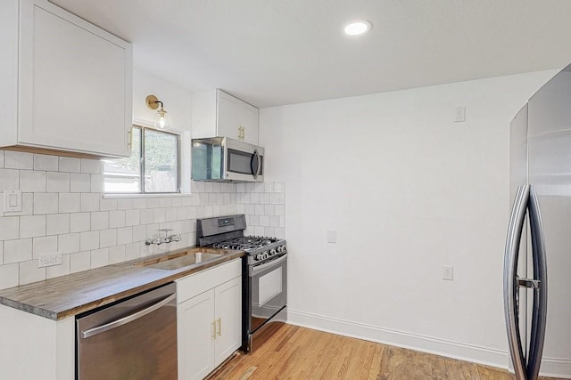 kitchen featuring tasteful backsplash, light wood-style flooring, appliances with stainless steel finishes, a sink, and baseboards