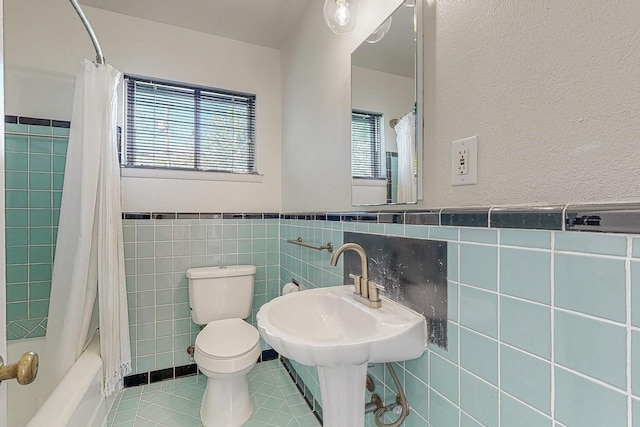 bathroom with tile patterned flooring, toilet, tile walls, wainscoting, and shower / bathtub combination with curtain