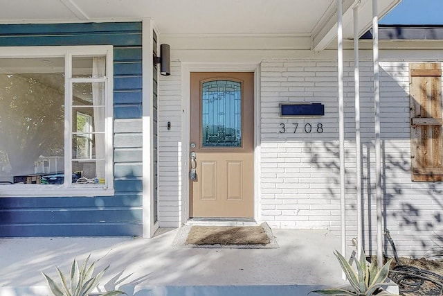 view of exterior entry with a porch and brick siding