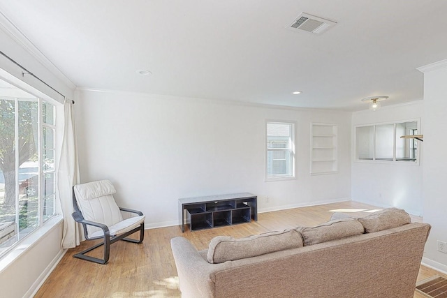 living area with a wealth of natural light, visible vents, crown molding, and light wood finished floors