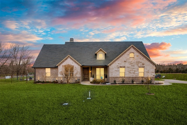 view of front of home with stone siding, fence, a front lawn, and roof with shingles