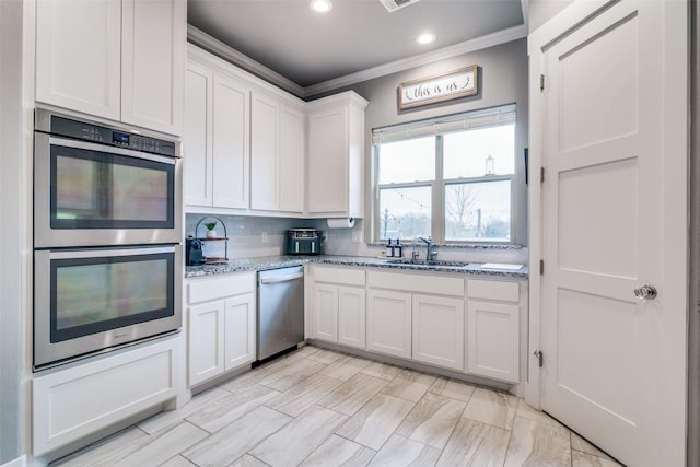 kitchen featuring decorative backsplash, white cabinets, appliances with stainless steel finishes, ornamental molding, and a sink