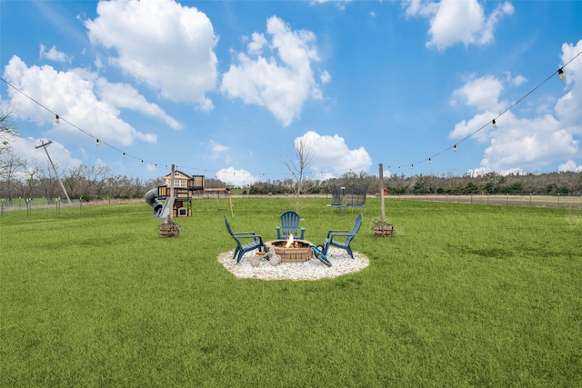 view of playground featuring a trampoline, a fire pit, and a lawn