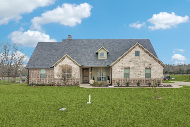 view of front of house with a shingled roof, stone siding, fence, a front yard, and brick siding