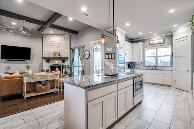 kitchen featuring stainless steel microwave, a kitchen island, stone counters, and a wealth of natural light