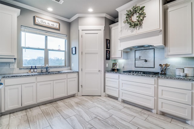 kitchen with gas stovetop, white cabinetry, a sink, and stone countertops