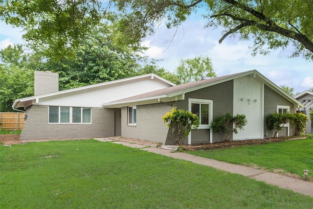 view of front of house featuring brick siding, a front lawn, a chimney, and fence