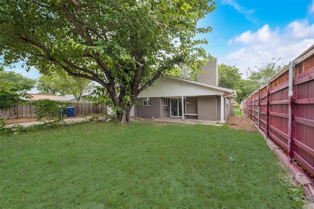 back of property featuring brick siding, fence, a lawn, a chimney, and a patio area