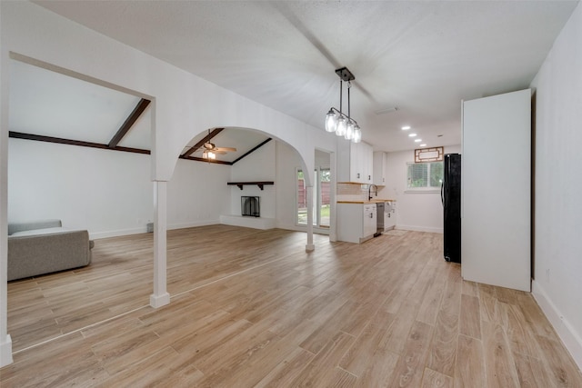 unfurnished living room featuring arched walkways, light wood finished floors, a fireplace with raised hearth, a sink, and ceiling fan