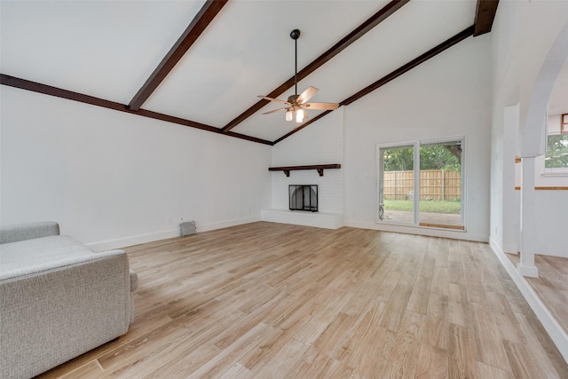 unfurnished living room with arched walkways, ceiling fan, light wood-style flooring, a fireplace, and beamed ceiling