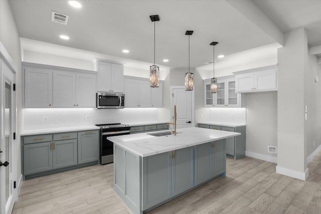 kitchen with gray cabinetry, appliances with stainless steel finishes, a sink, and decorative backsplash