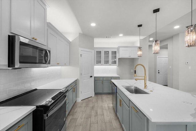 kitchen with backsplash, appliances with stainless steel finishes, white cabinetry, a sink, and light wood-type flooring