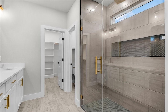 bathroom featuring a stall shower, a walk in closet, vanity, and baseboards