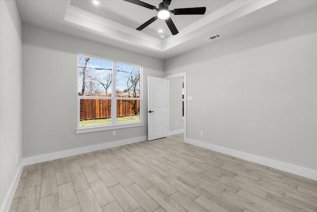 spare room with light wood-style floors, baseboards, visible vents, and a raised ceiling