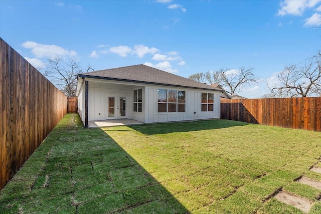 rear view of house with a fenced backyard, a shingled roof, a yard, french doors, and board and batten siding