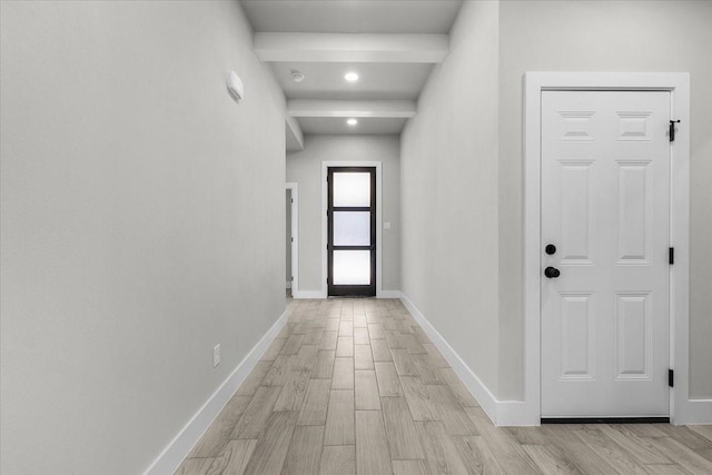 corridor with light wood-style floors, baseboards, and beamed ceiling