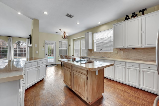 kitchen featuring light countertops, visible vents, backsplash, a kitchen island, and a sink