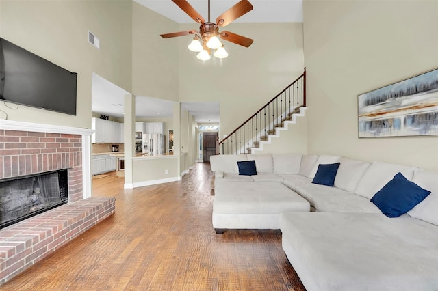 living area with a ceiling fan, visible vents, stairs, light wood-style floors, and a brick fireplace