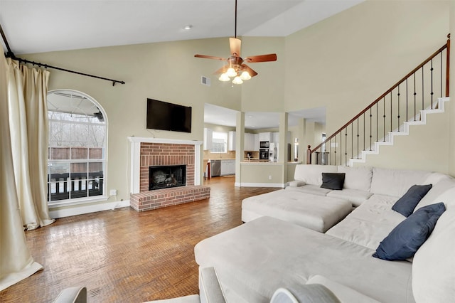 living room with a wealth of natural light, a brick fireplace, ceiling fan, and stairway