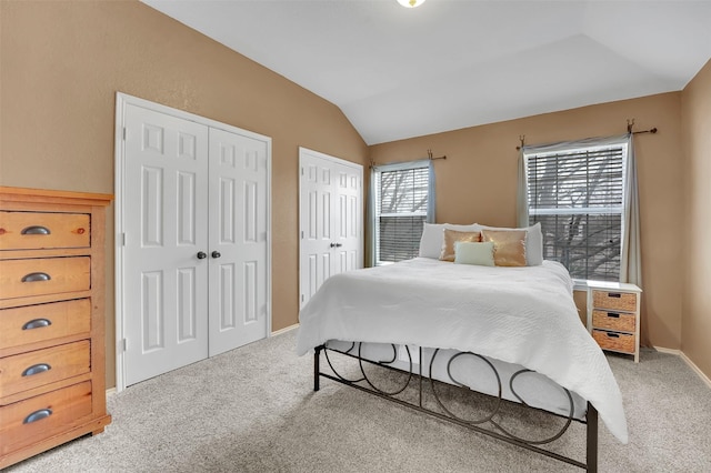 bedroom with multiple closets, light colored carpet, vaulted ceiling, and baseboards