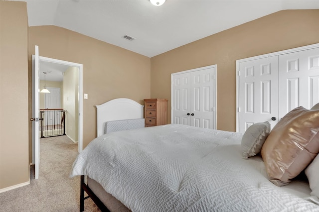 carpeted bedroom with lofted ceiling, baseboards, visible vents, and two closets