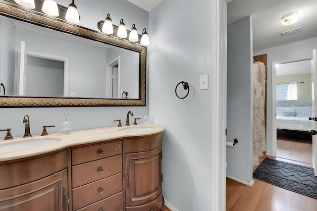 ensuite bathroom with double vanity, visible vents, connected bathroom, wood finished floors, and a sink