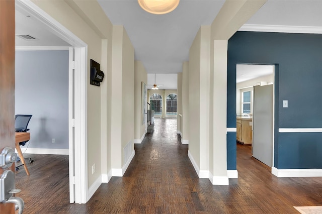 hall featuring dark wood-type flooring, visible vents, crown molding, and baseboards