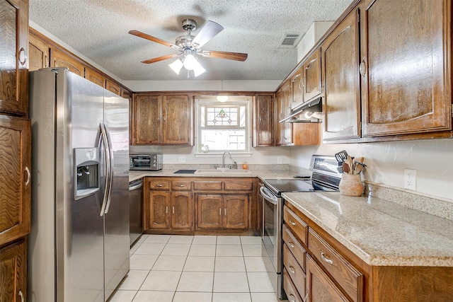 kitchen featuring appliances with stainless steel finishes, brown cabinetry, a sink, and under cabinet range hood