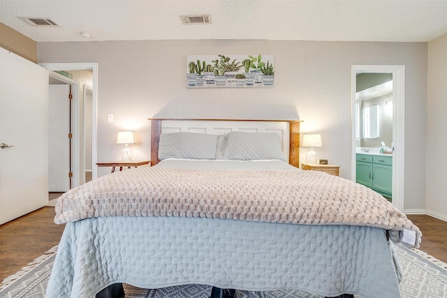 bedroom featuring visible vents, a textured ceiling, baseboards, and wood finished floors