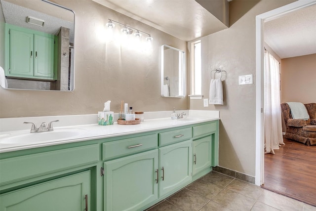 full bathroom with double vanity, tile patterned flooring, a textured ceiling, and a sink