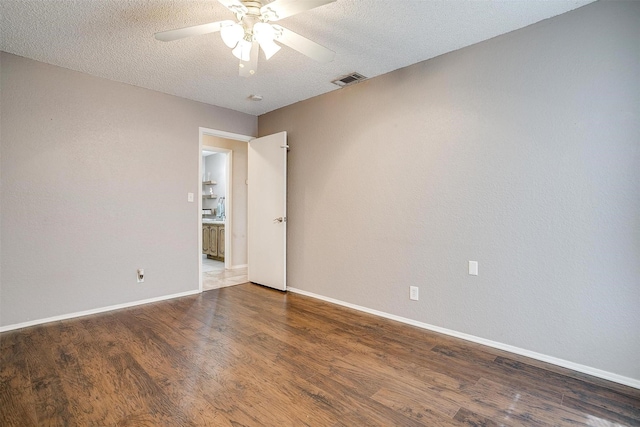 empty room with a textured ceiling, wood finished floors, a ceiling fan, visible vents, and baseboards