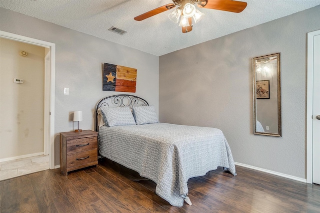 bedroom with a textured ceiling, wood finished floors, visible vents, and baseboards