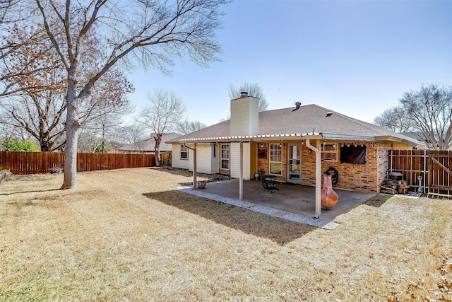 rear view of property with brick siding, a chimney, a shingled roof, a patio area, and a fenced backyard