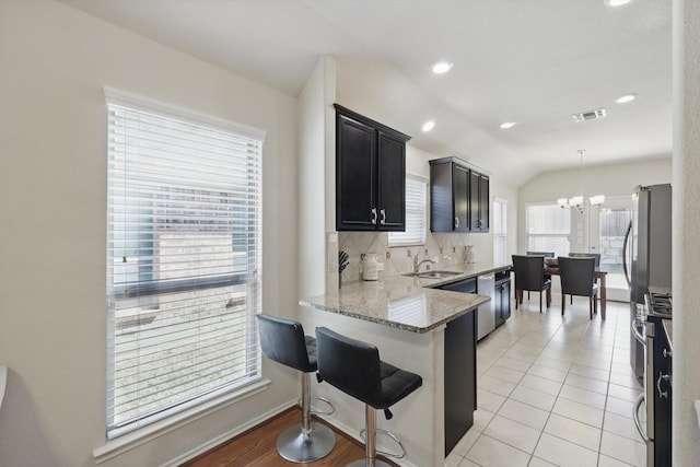 kitchen featuring light stone counters, lofted ceiling, decorative backsplash, a sink, and dishwasher