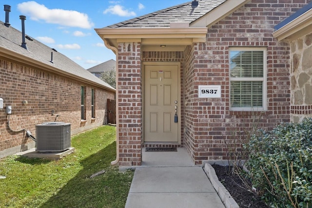 view of exterior entry featuring a yard, brick siding, and central air condition unit