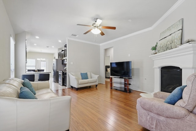 living area featuring ornamental molding, a glass covered fireplace, visible vents, and light wood-style floors