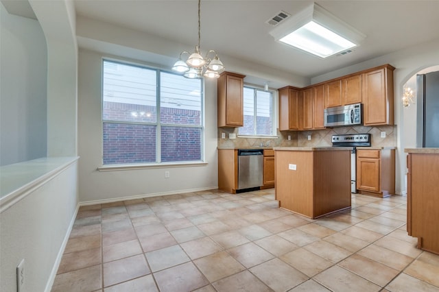 kitchen with visible vents, a kitchen island, arched walkways, appliances with stainless steel finishes, and tasteful backsplash