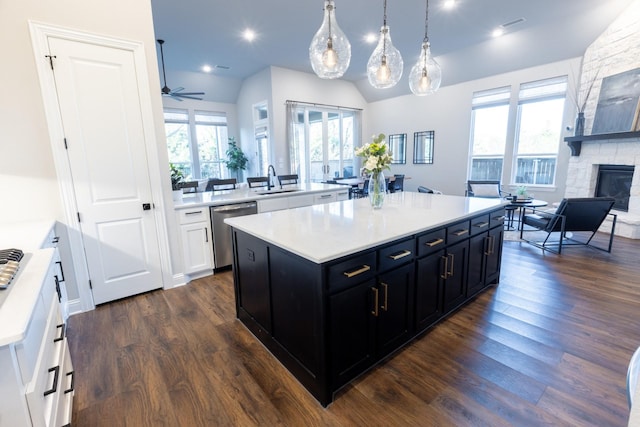 kitchen featuring a kitchen island, a fireplace, light countertops, stainless steel dishwasher, and dark cabinets