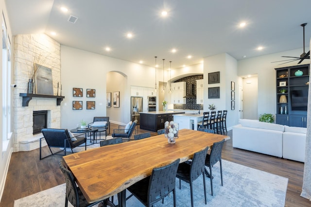 dining area featuring wood finished floors, visible vents, a fireplace, arched walkways, and vaulted ceiling