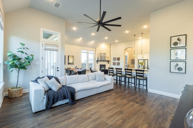 living room featuring visible vents, dark wood finished floors, a fireplace, arched walkways, and ceiling fan