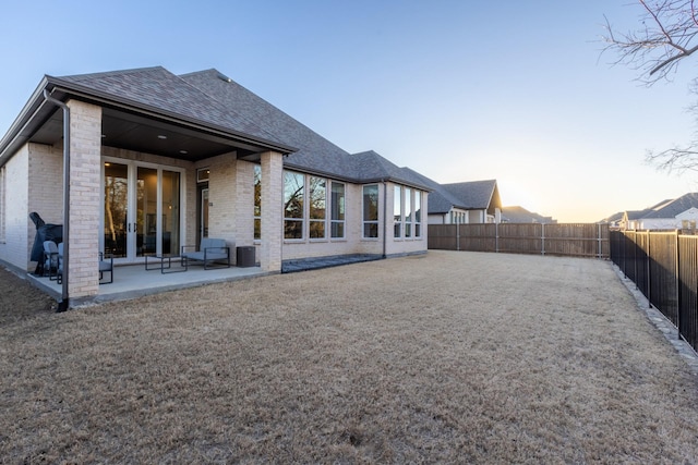 back of property with brick siding, roof with shingles, a fenced backyard, and a patio area