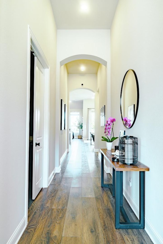 hall featuring hardwood / wood-style flooring, arched walkways, and baseboards